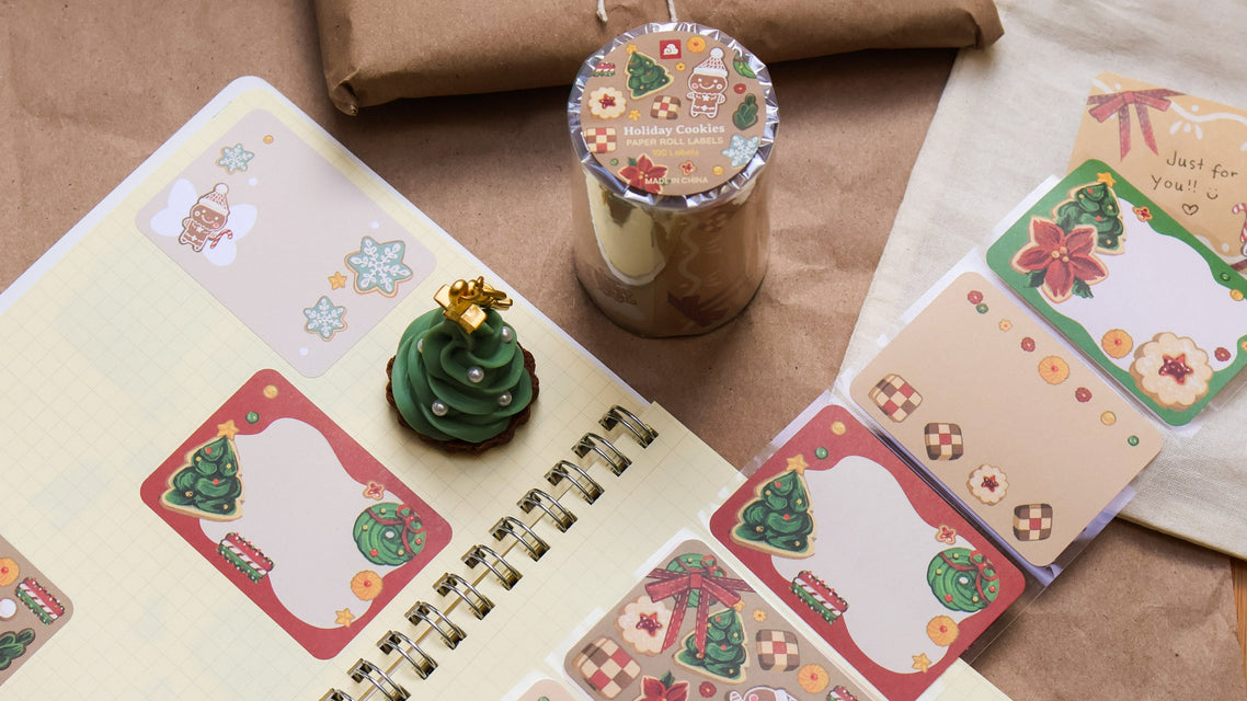 Notebook with Christmas-themed stickers, a small green tree decoration, and a wrapped gift on a brown surface.
