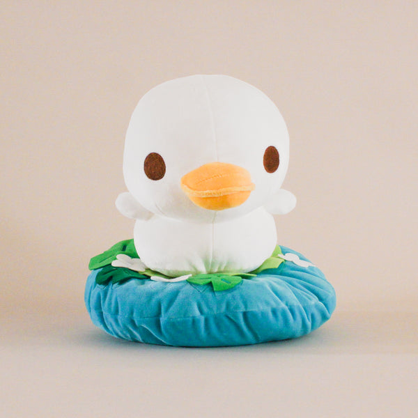 A cute duckling plushie, size large, swimming in a pond with lily pads and small flowers